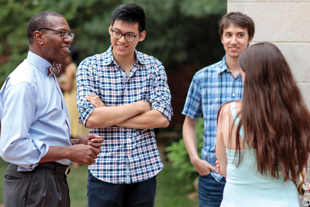 Will Ross talks with a group of smiling medical students outside his home.